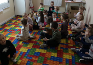 Dzieci siedza na dywanie w sali multimedialnej