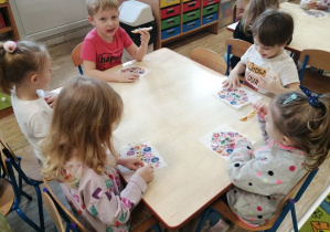 Dzieci siedzą przy stolikach i wykonujapracę plastyczną